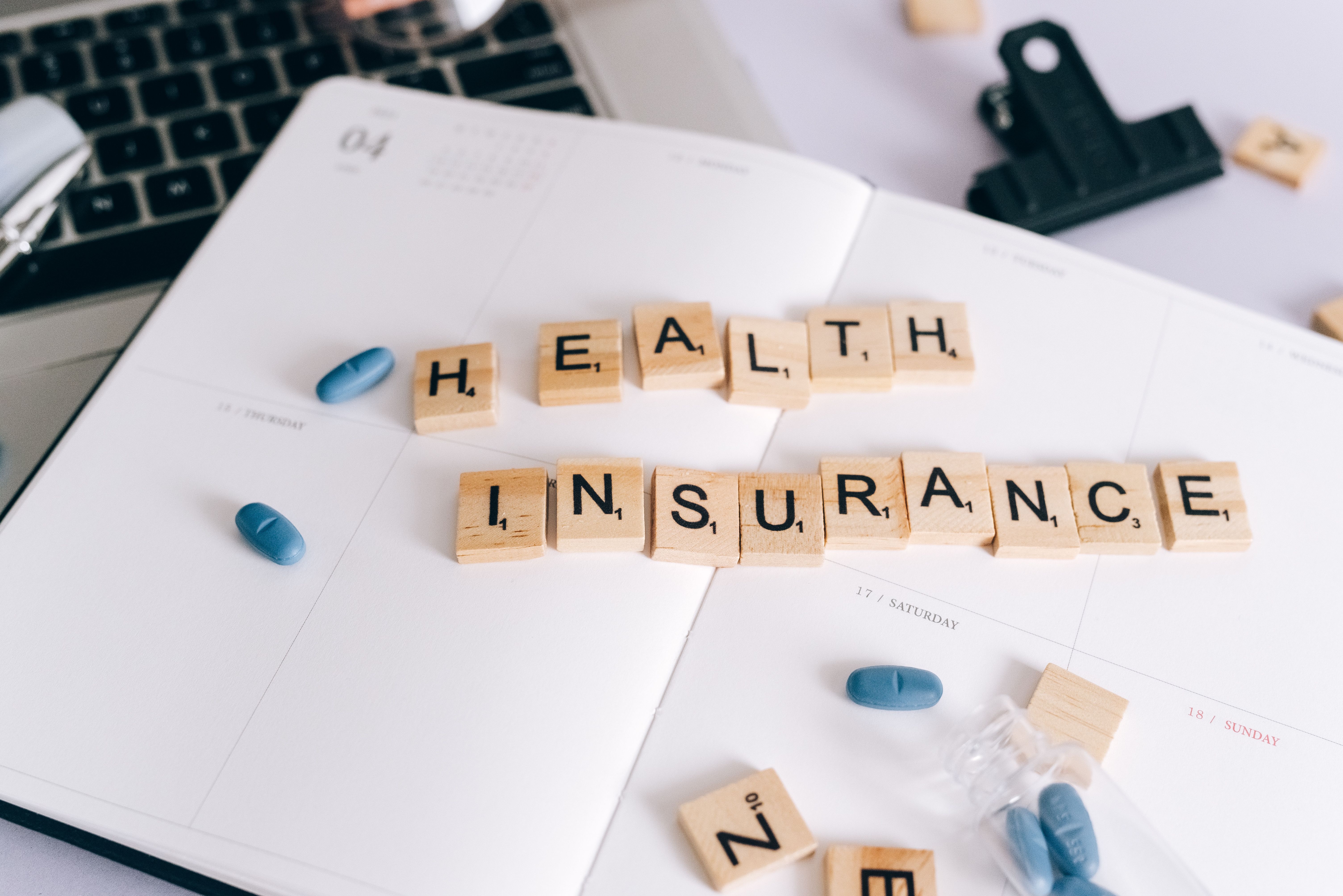 Peças de madeira escrevem "health insurance" ao lado de comprimidos, representando a escolha do melhor plano de saúde.