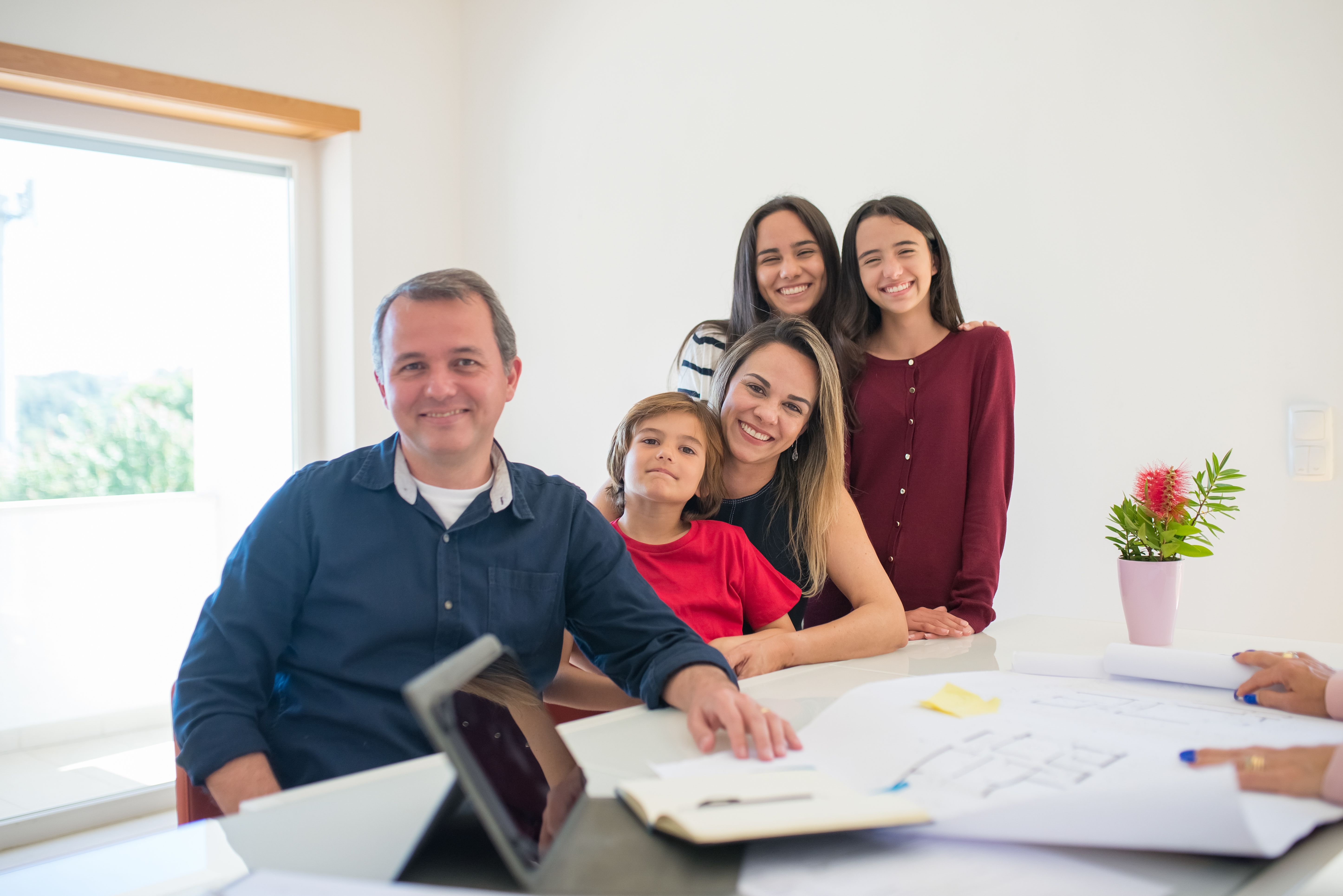 Família reunida e sorrindo à mesa, com tablet e documentos, decidindo entre plano de saúde individual e familiar.