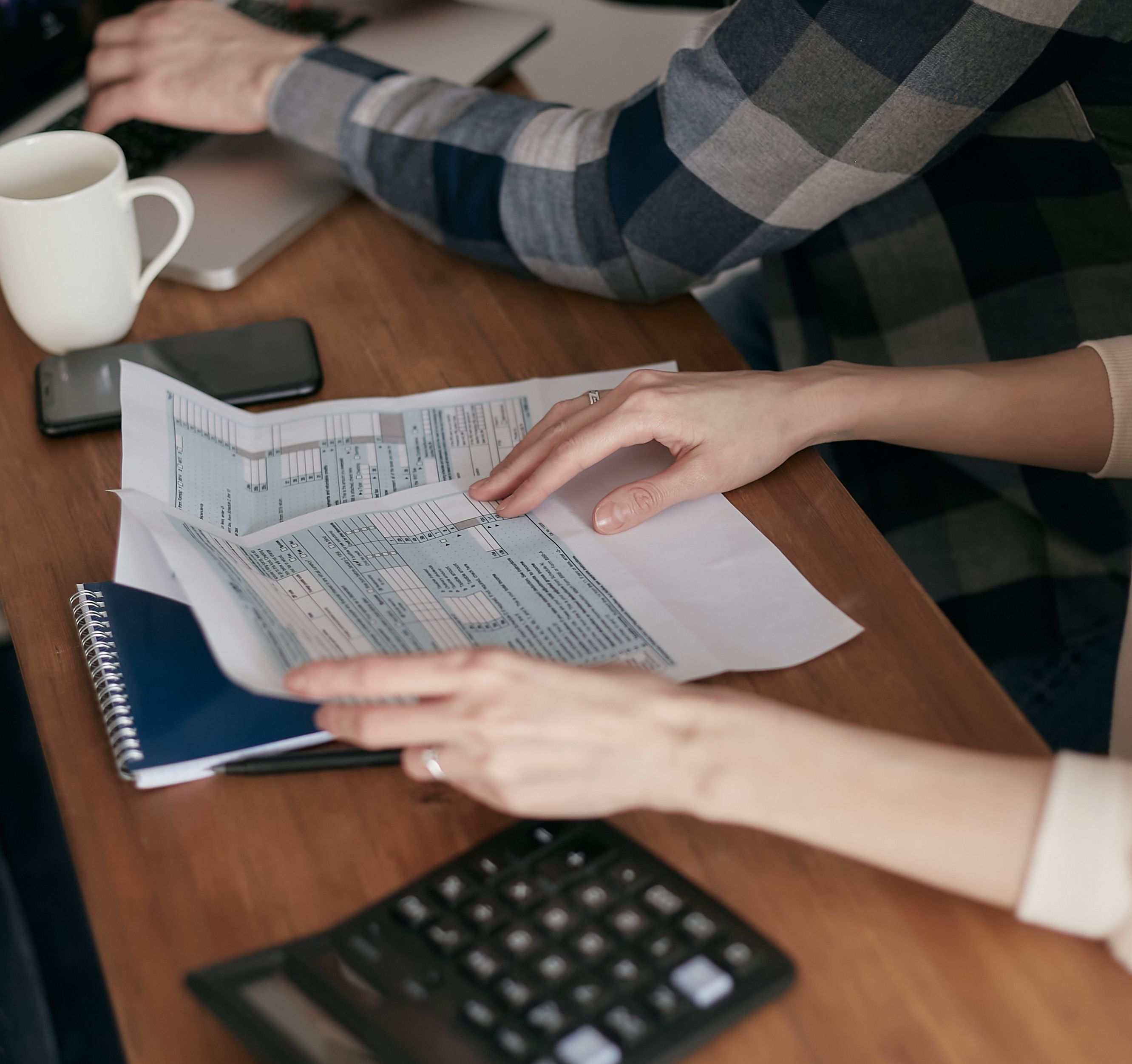 Duas pessoas analisando documentos com uma calculadora na mesa, comparando preços de planos de saúde familiares.