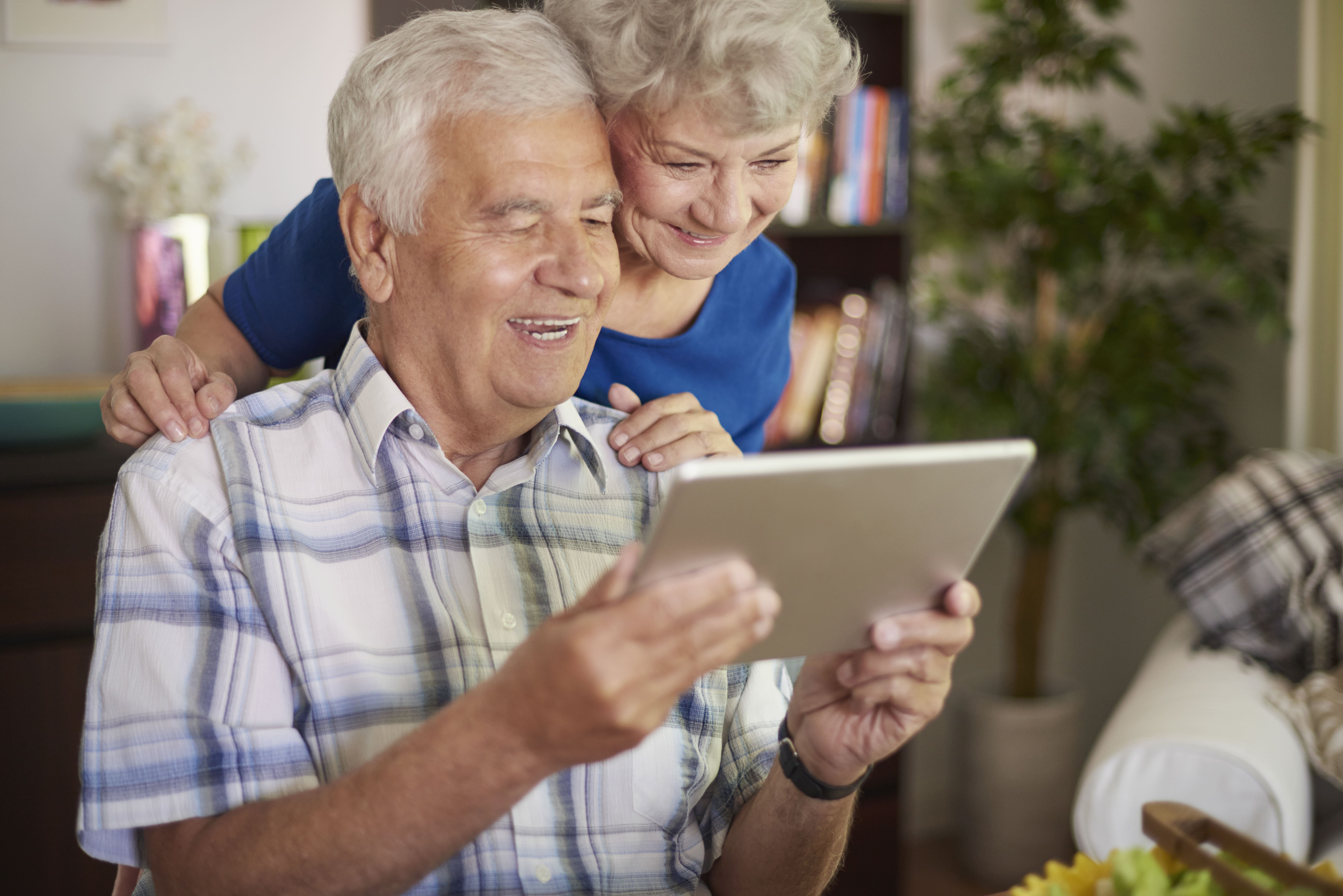 Casal de idosos sorri enquanto pesquisa informações sobre plano de saúde em um tablet em casa
