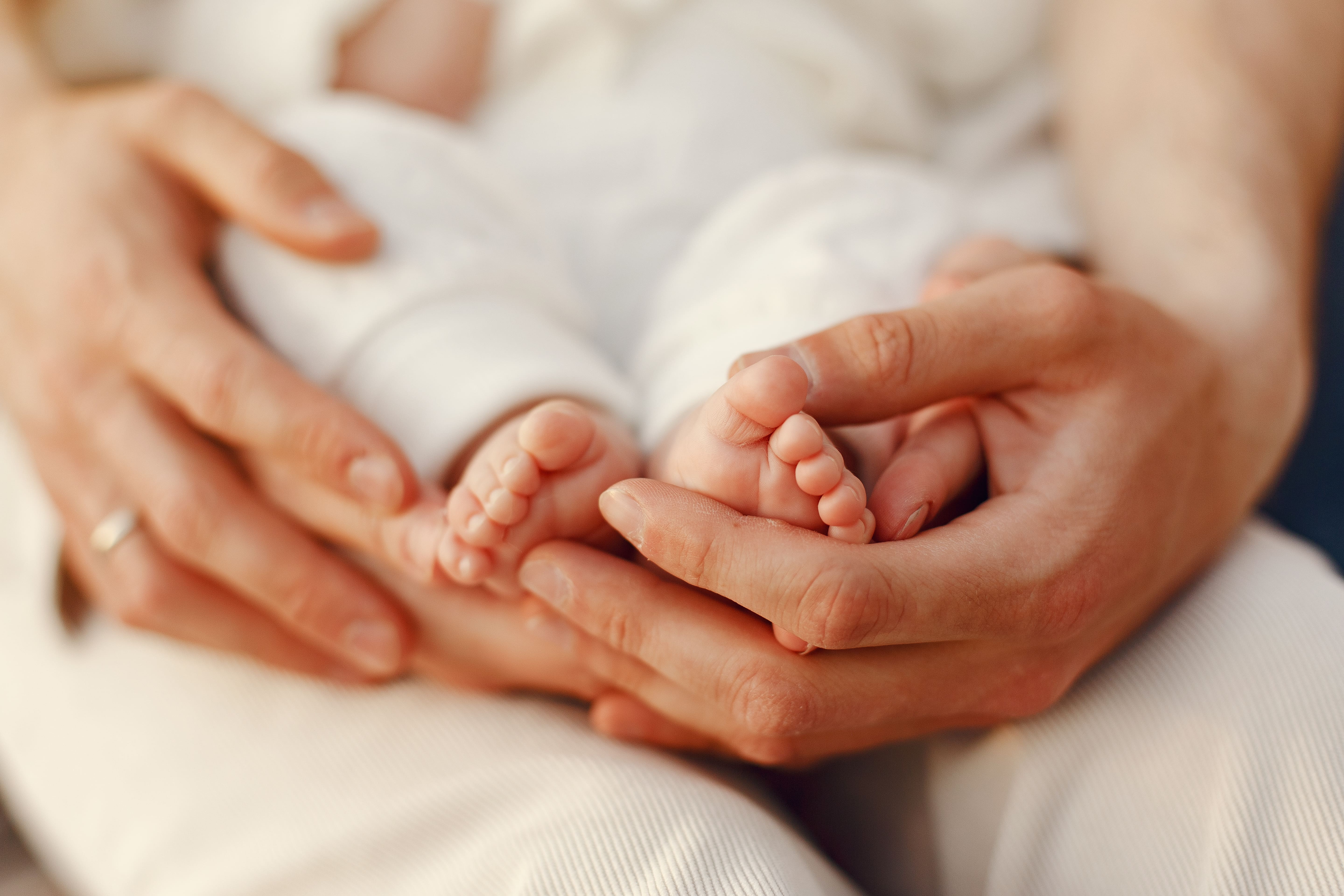 Mãos dos pais segurando os pés de um bebê recém-nascido.
