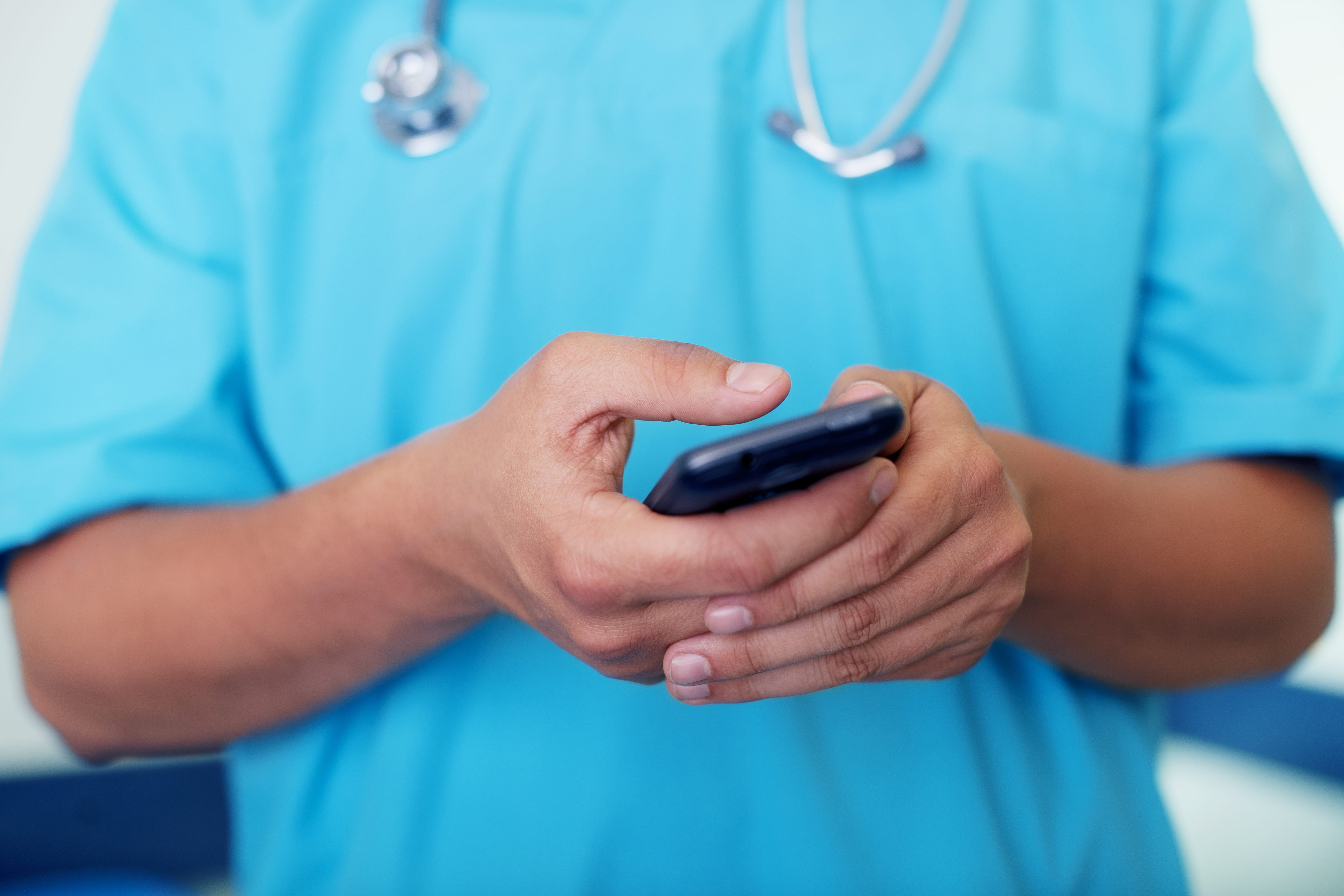 Profissional de saúde de jaleco azul e estetoscópio usando o celular para consultar informações sobre plano de saúde