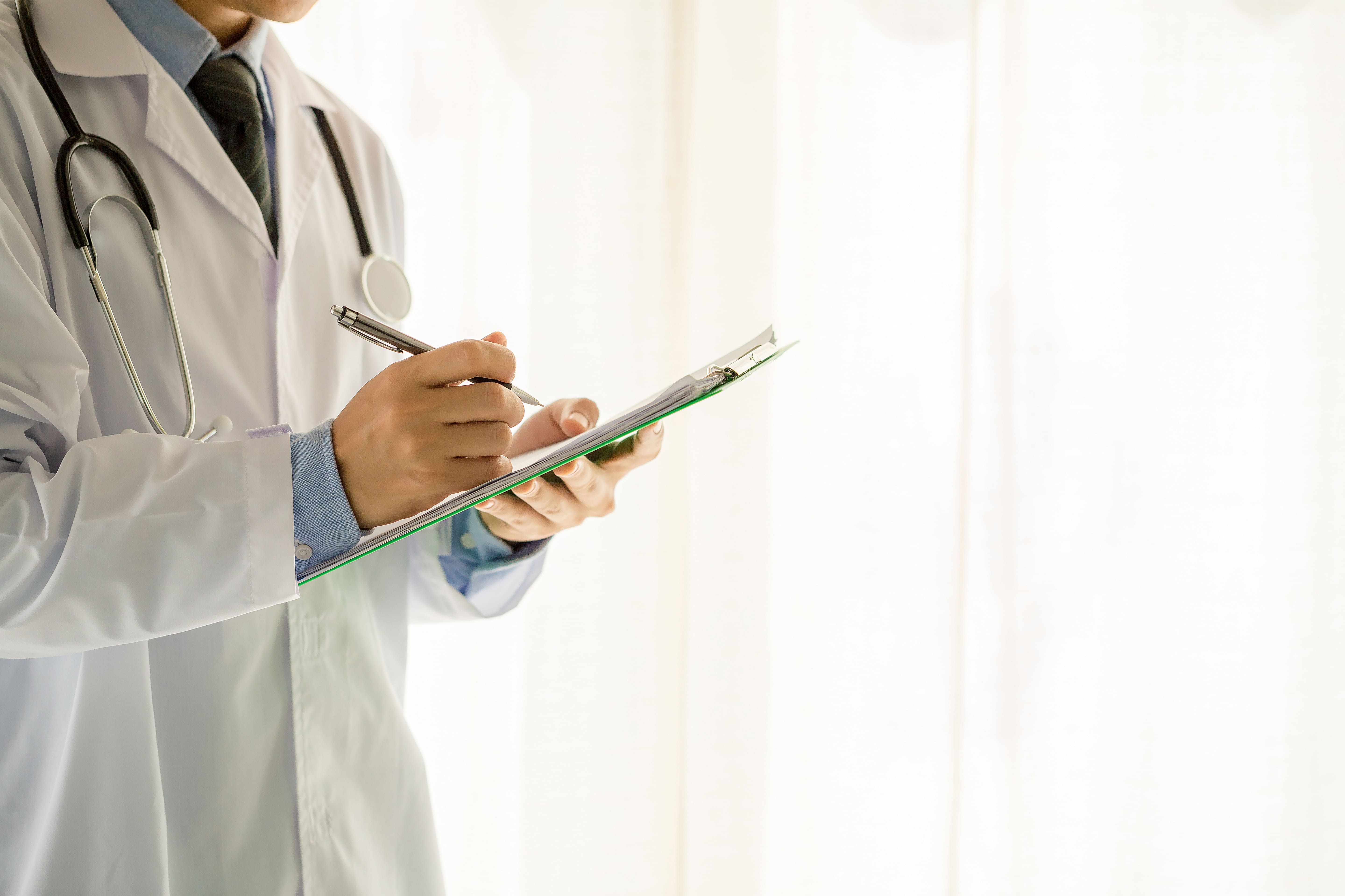 Médico de jaleco branco e estetoscópio anotando em uma prancheta, representando a escolha de um plano com boa rede de exames