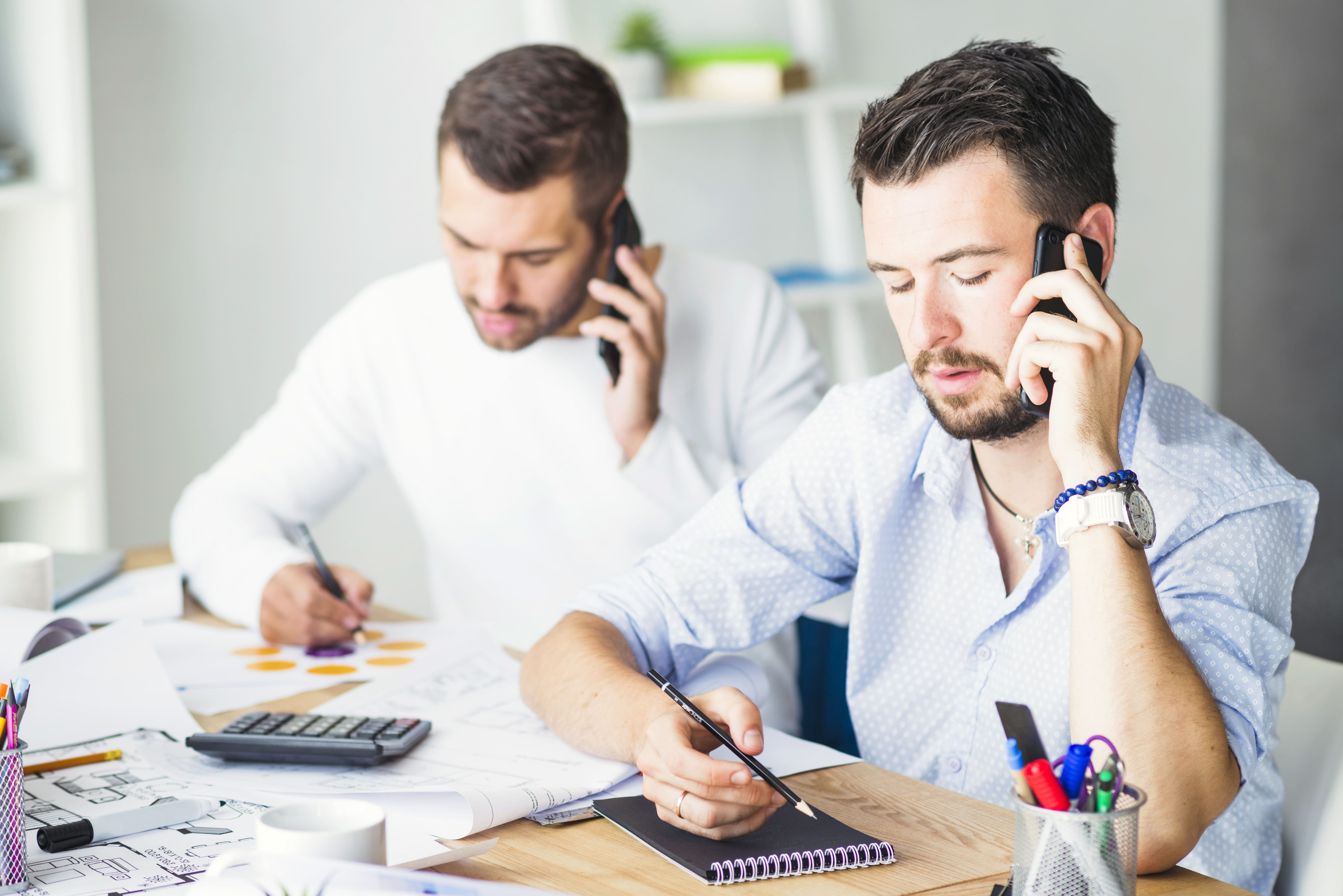 Dois homens ao telefone anotando informações enquanto analisam documentos para trocar de plano de saúde