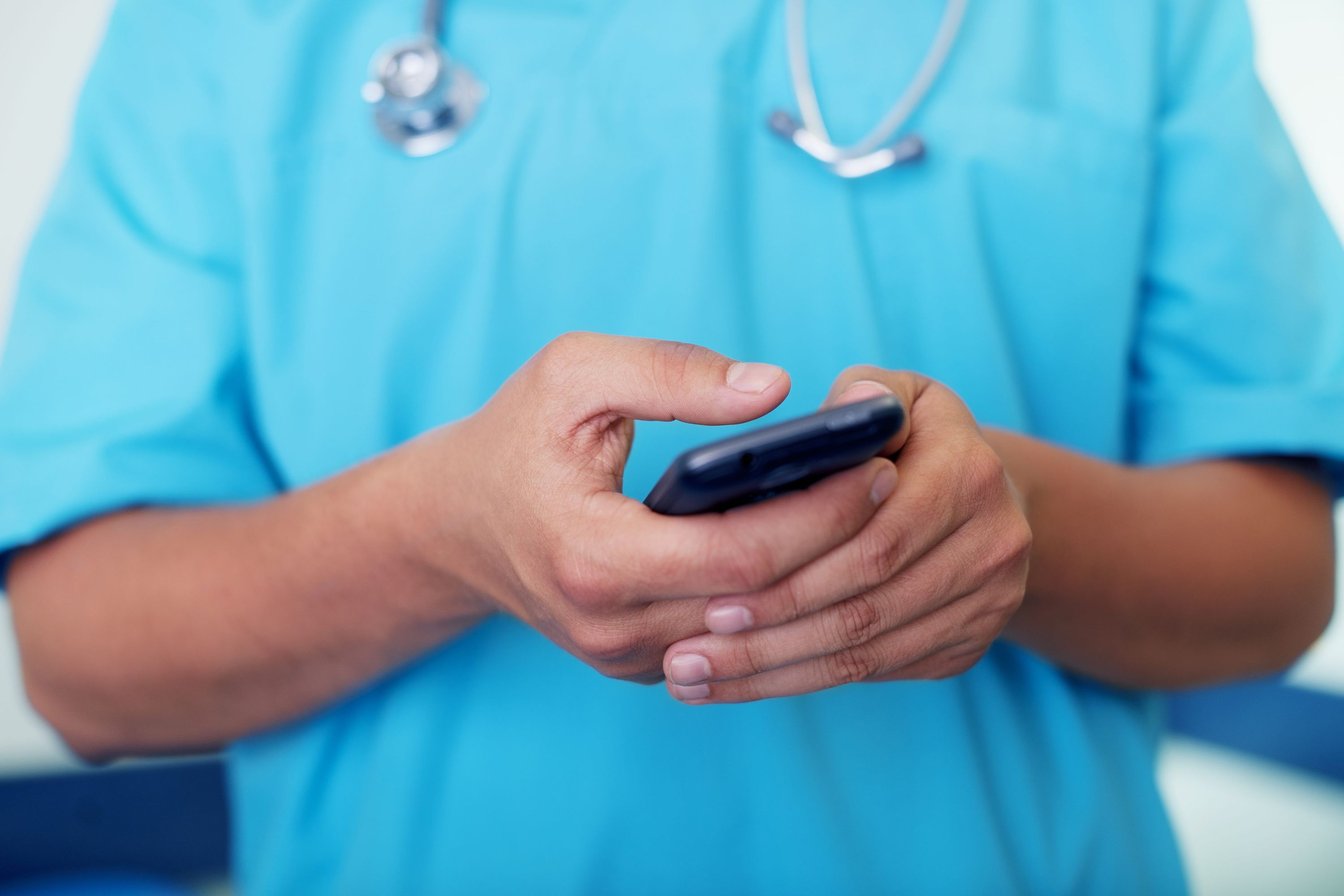 Profissional de saúde de jaleco azul e estetoscópio usando o celular para consultar informações sobre plano de saúde